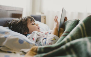 Young child laying in bed and using a tablet device