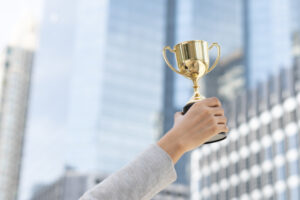 woman's hand holding gold trophy cup against backdrop of city skyscrapers. Women in business