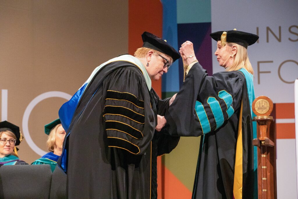 Dr. Schornack bows to get cords placed over her academic robes during her inauguration as president