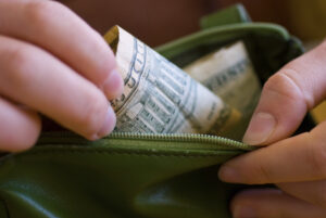 photo shows woman taking paper money out of a green wallet 