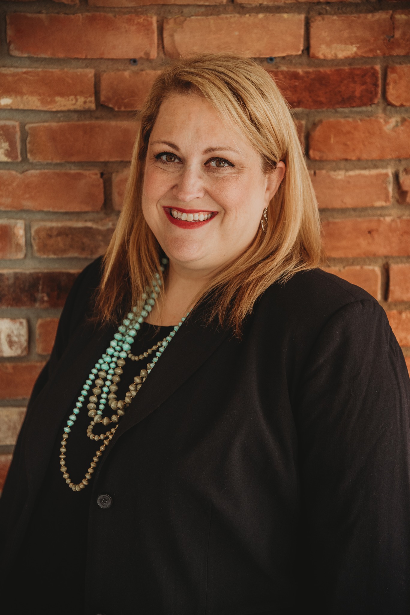 portrait of nikie walker, an HR consultant for optometrists. She is standing against a brick wall,. 