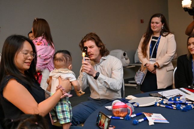 student looks at infant's eyes while mom holds baby. Infantsee pop up trainings give young doctors and students opportunity to work with infants