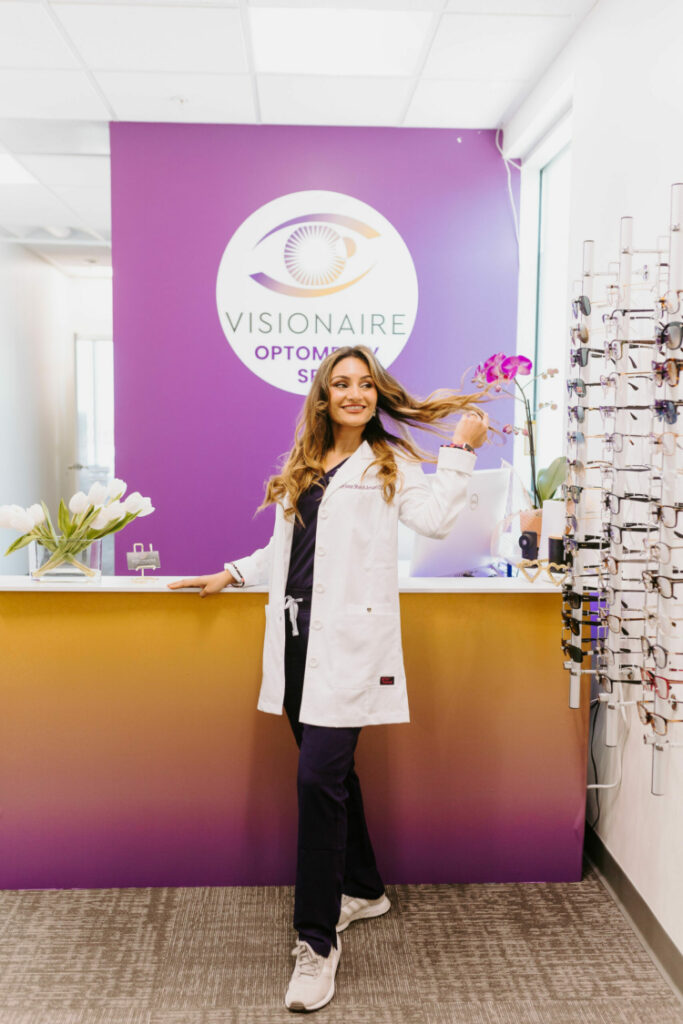 Dr. Shakil at her front desk, in front of her puple logo for her practice and med-spa