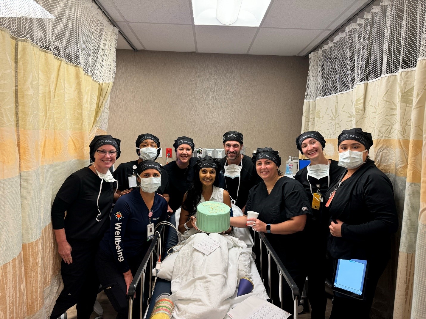 Dr. Virani sits up in surgical bed after her EVo ICL procedure. The surgical team is around her with cake