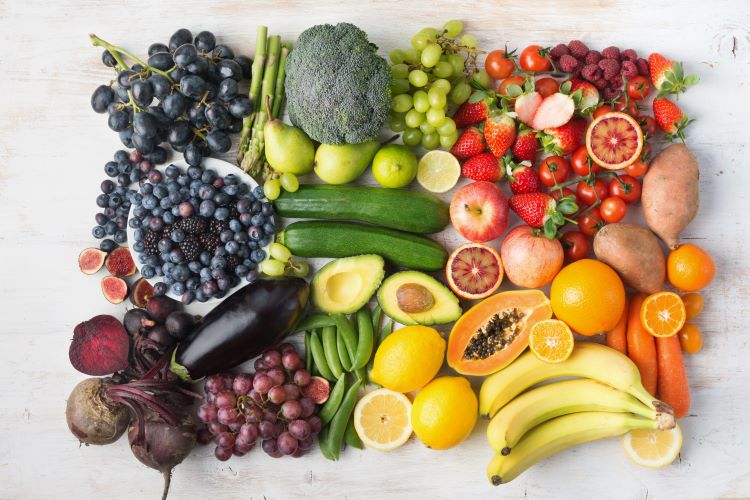 array of colorbful food - blues and purples are berries and radishes, eggplants, greens are broccoli and avocadoes, reds are pomegranates and berries, oranges are yams and carrots and yellows are lemons and bananas
