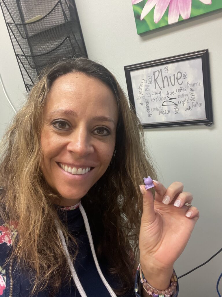Dr. Brianna Rhue holding a plastic purple frog between thumb and index finger