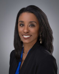 Dr. Ashley Tucker in blue blouse, black blazer against a gray background